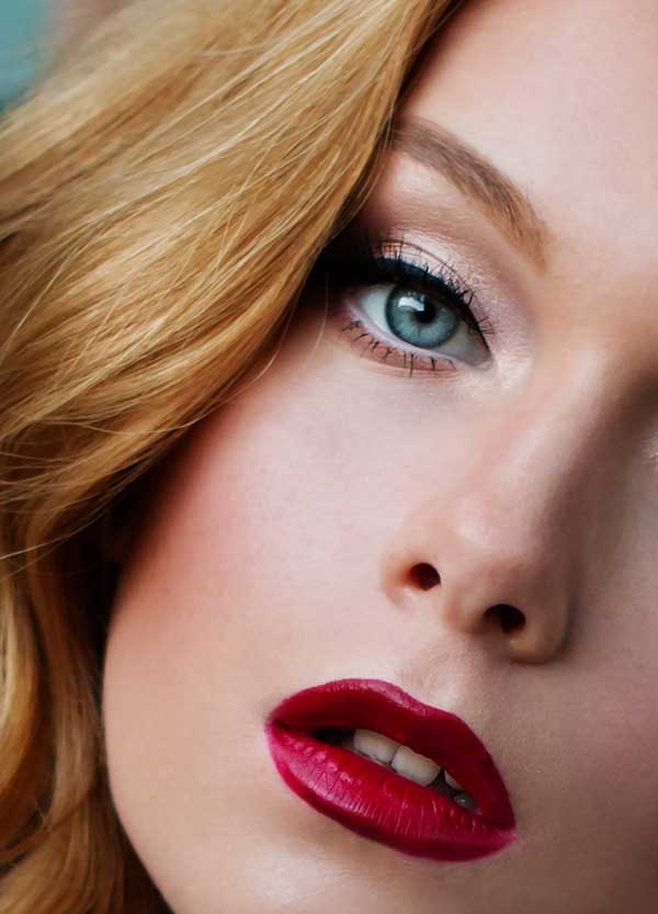 Close-up of a woman with glam makeup, bold red lipstick, defined eyes, and highlighted skin after makeup application.