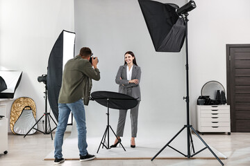 A photographer taking pictures of a woman posing in a studio setup with lighting equipment during a professional photoshoot session.