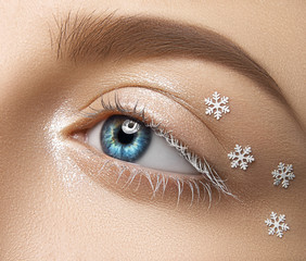 Close-up of a beautifully styled eye with shimmer makeup and small snowflake decorations, showcasing creative eye makeup artistry.