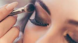 Makeup artist applying eyeshadow with a brush on a closed eyelid.